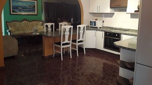 Cuina compacta amb armaris blancs, microones i un rentaplat. Zona de dinar amb sofà i cadires.