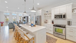 A spacious kitchen with white cabinetry, a large island with bar stools, stainless steel appliances, and pendant lighting. - Designer Cinnamon Shore Condo w/ Charm+Easy Access to Countless Amenities! (Port Aransas)