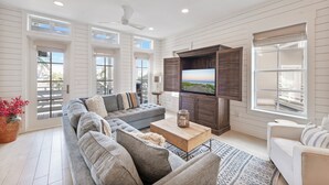 A spacious living room with a large gray sectional sofa, a wooden coffee table, and a TV mounted on a wooden wall. - Designer Cinnamon Shore Condo w/ Charm+Easy Access to Countless Amenities! (Port Aransas)