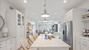 A modern kitchen with white cabinetry, a central island, and a stainless steel refrigerator. - Designer Cinnamon Shore Condo w/ Charm+Easy Access to Countless Amenities! (Port Aransas)