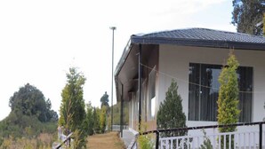 A two-story house with a covered porch, a stone retaining wall, and a white fence. - Katyuri Nature View Resort (Lansdowne)