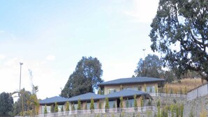 A building with multiple levels, a stone retaining wall, and a pathway leading to the entrance. - Katyuri Nature View Resort (Lansdowne)