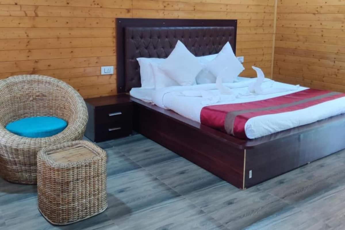 Ein Zimmer mit Holzwänden, einem Bett, zwei Korbstühlen und einem Nachttisch.