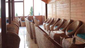 A row of wicker chairs with blue cushions in a room with wooden walls and large windows. - Katyuri Nature View Resort (Lansdowne)