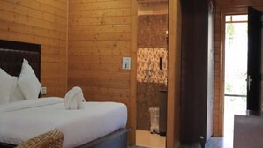 A wooden cabin room with a bed, a small bathroom, and a wooden door leading outside. - Katyuri Nature View Resort (Lansdowne)