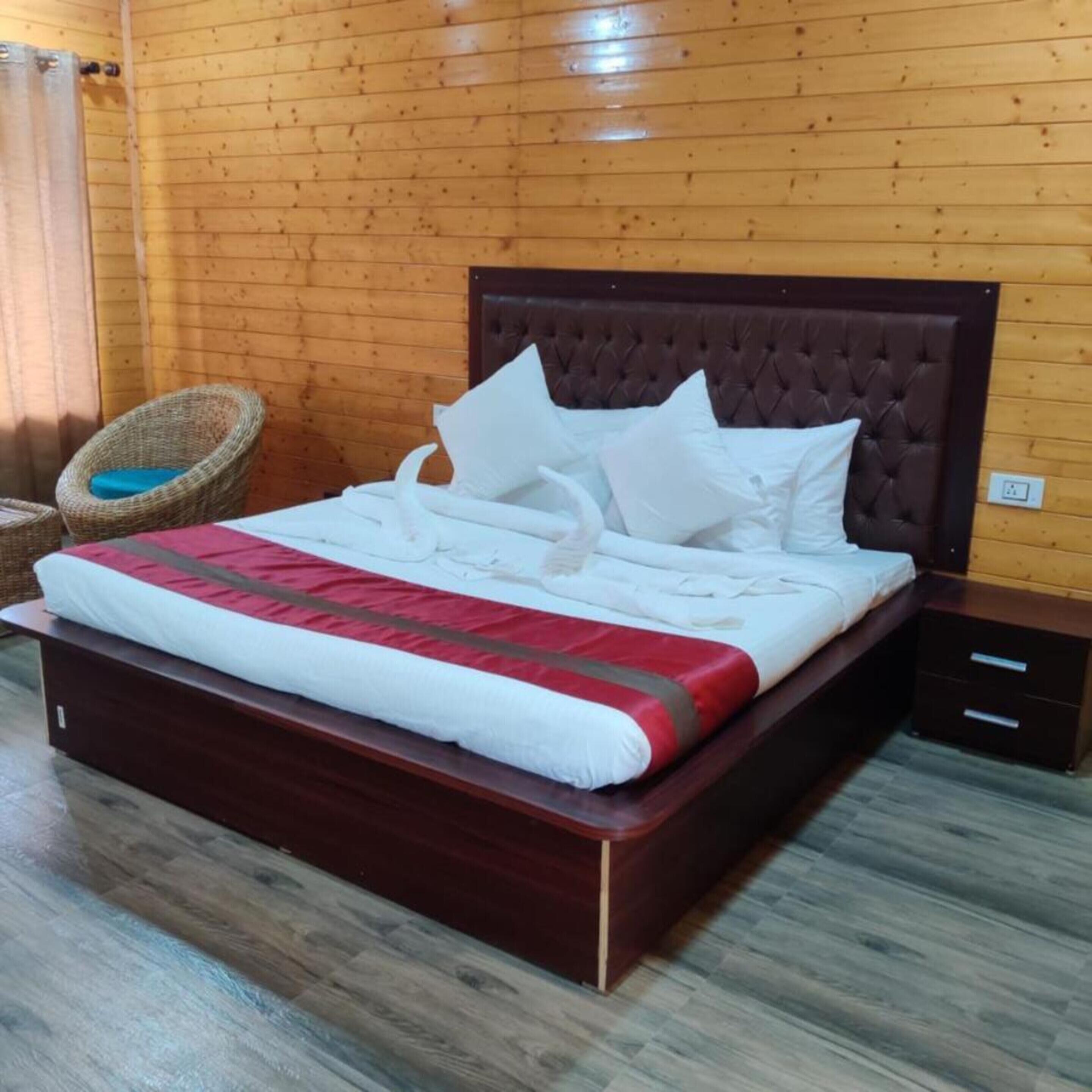 A wooden-paneled room with a bed, a nightstand, and a wicker chair.
