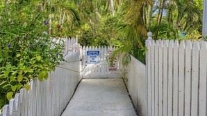 A pathway leading to a swimming pool with a white picket fence, surrounded by lush greenery and palm trees. - A Key West State Of Mind at The Key West Golf Club (Key West)