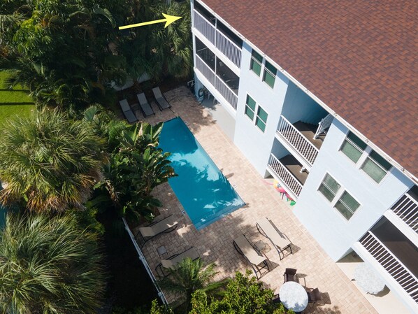 An aerial view of a hotel with a swimming pool, lounge chairs, and a garden area.