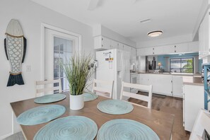 A modern kitchen with white cabinets, a built-in refrigerator, and a dining area with a wooden table and blue placemats. - SeaDuction of Anna Maria Island (Holmes Beach)