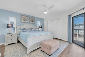 A bedroom with a bed, nightstands, a ceiling fan, artwork on the wall, and a view through a window. - SeaDuction of Anna Maria Island (Holmes Beach)