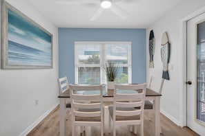 A dining area with a table and four chairs, a ceiling fan, a window with blinds, and a painting on the wall.