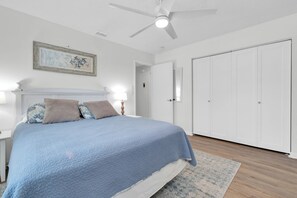 A bedroom with a bed, nightstands, a ceiling fan, a door, and a framed picture on the wall.