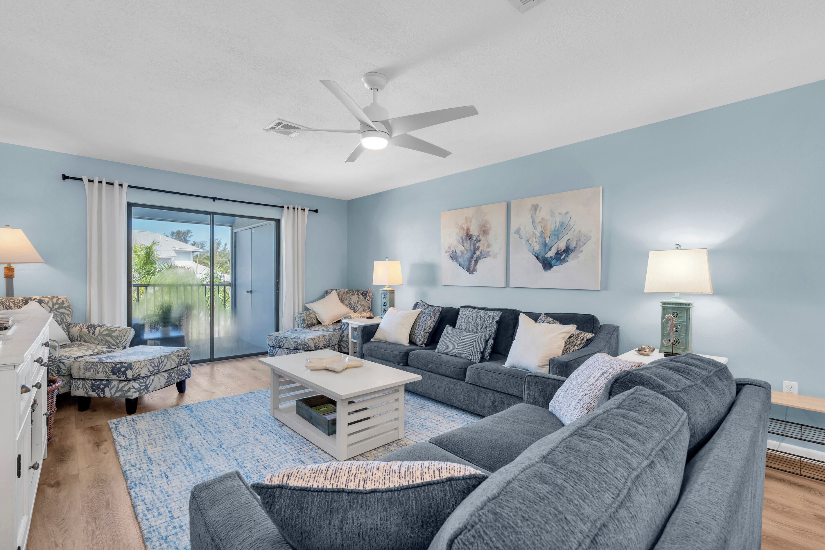 A living room with a ceiling fan, two sofas, a coffee table, and a large window with curtains.