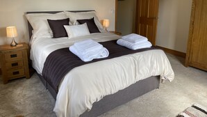 A neatly made bed with pillows, a bedside lamp, a folded towel, and a wooden wardrobe. - Countryside Bungalow with private Hot Tub (Llansteffan (6.6miles N))
