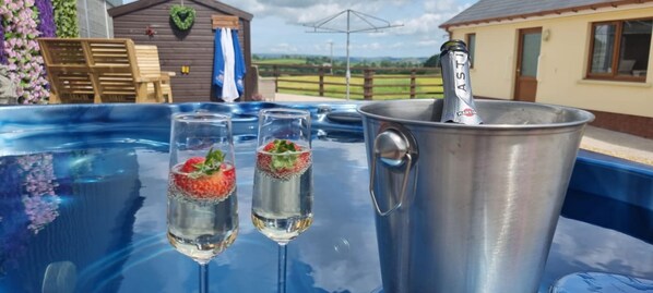 Een jacuzzi met twee champagneglazen, een metalen emmer met een fles, houten stoelen en een huis op de achtergrond.