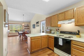 Une cuisine avec des meubles de rangement en bois, une cuisinière et un coin repas comprenant des chaises et une table.