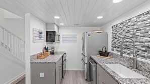 A modern kitchen with granite countertops, stainless steel appliances, and a tiled backsplash. - Beach House - Sky’s the Limit (Panama City Beach)