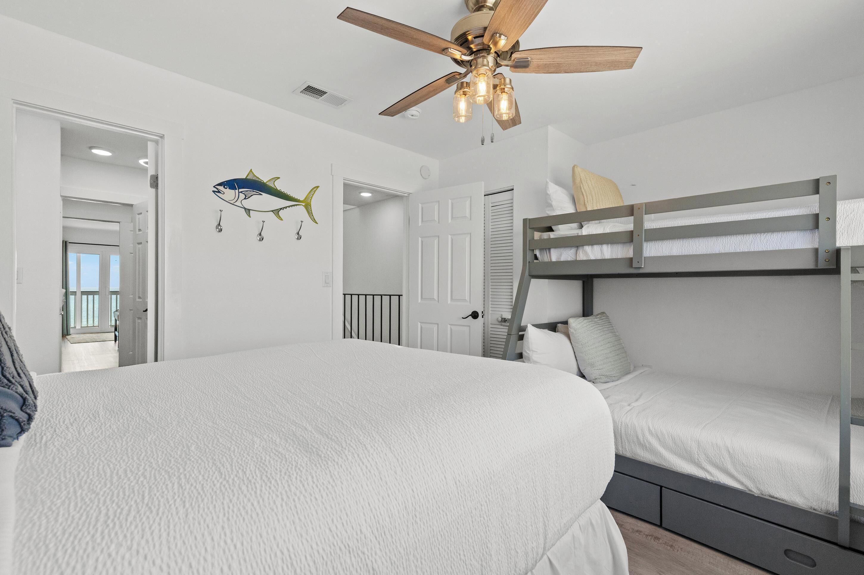 A bedroom with a bunk bed, a ceiling fan, and a door leading to another room.