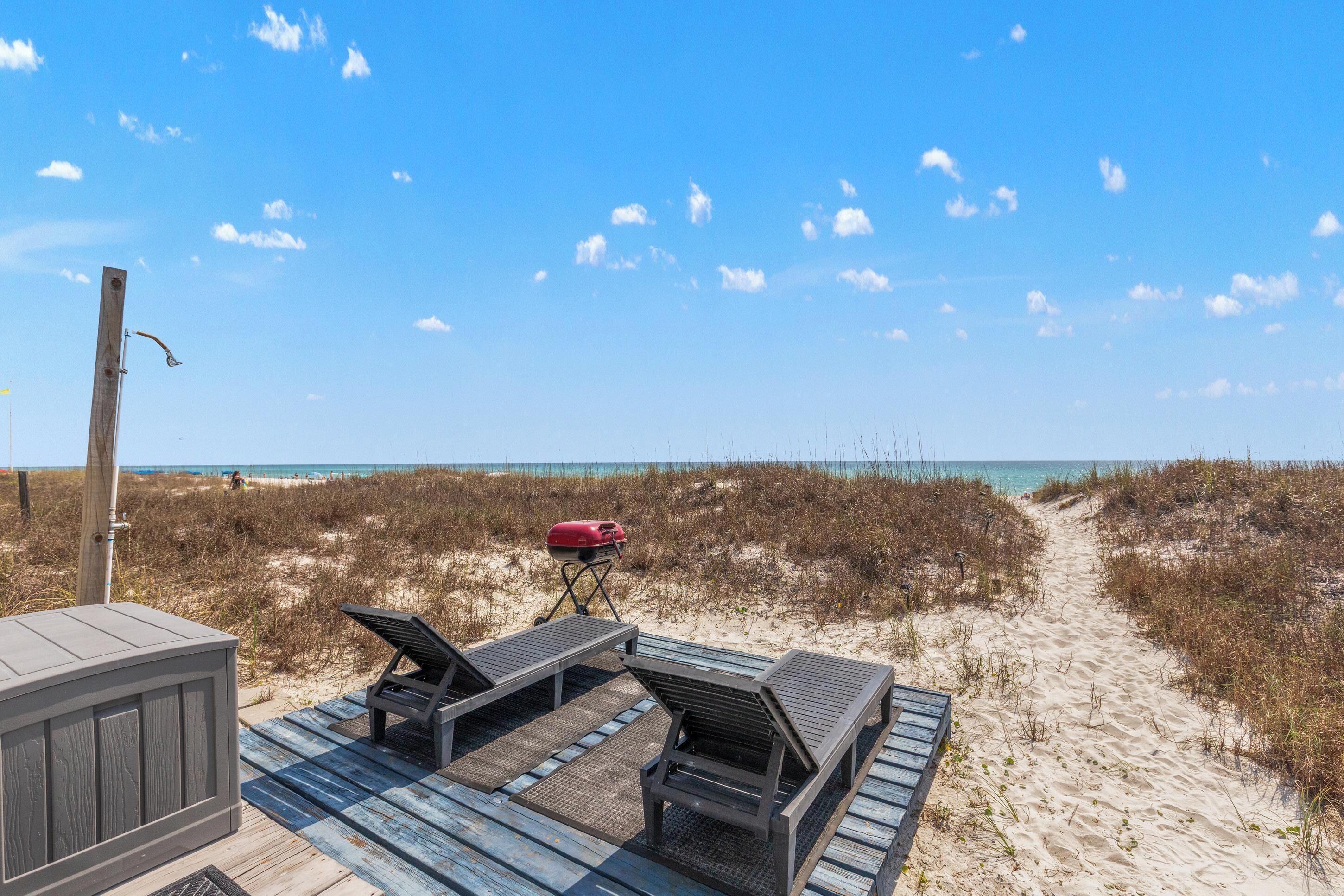 Een terras aan het strand met ligbedden, een barbecue en een houten blokhut.