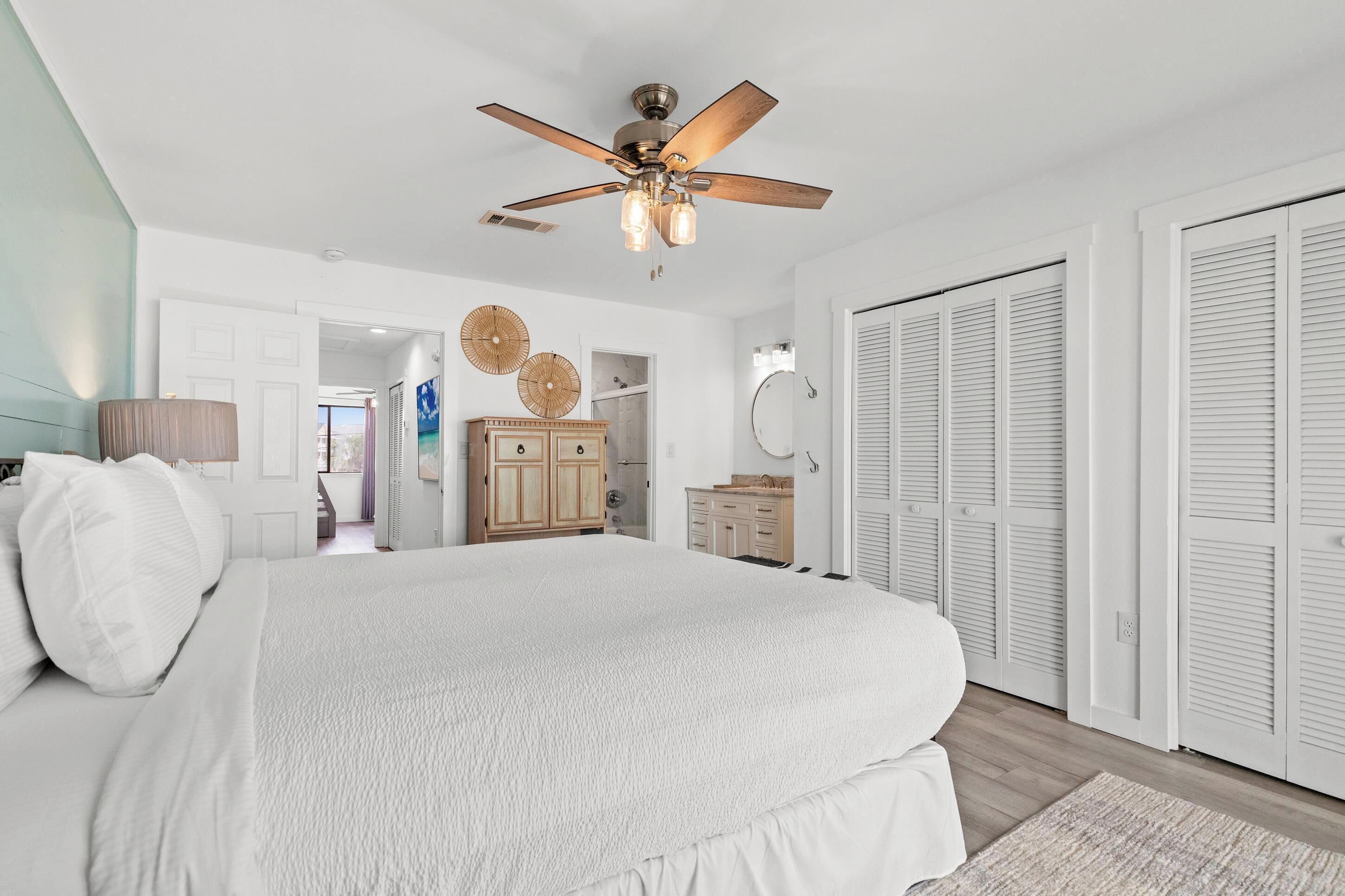 Un dormitorio con una cama grande, ventilador de techo, armarios de madera y closets blancos.
