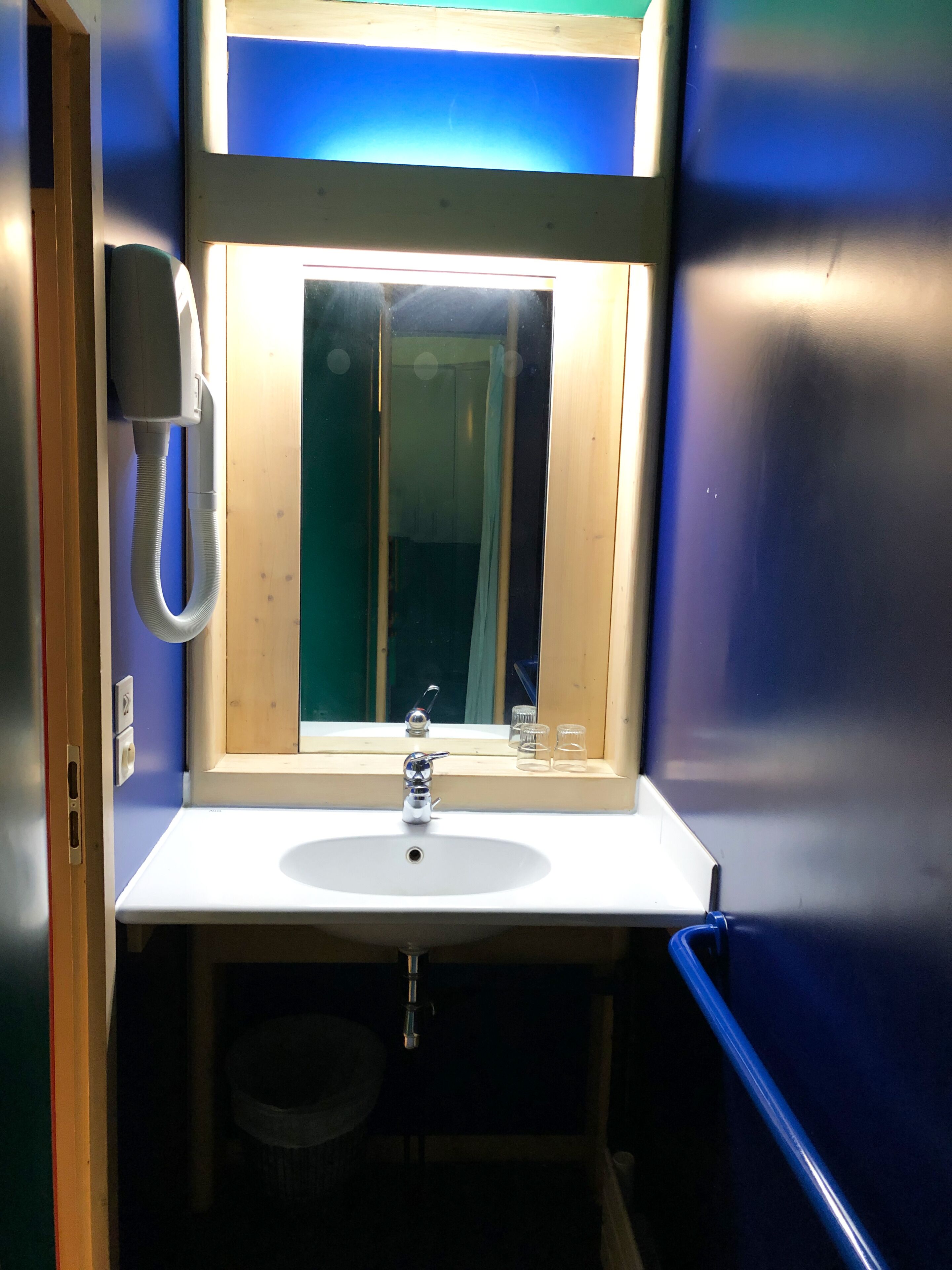 Un baño pequeño con un lavamanos blanco, un espejo y un teléfono.