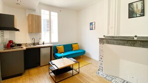 Un espacio habitable compacto con kitchenette, un sofá azul con cojines amarillos, una mesita y una chimenea.
