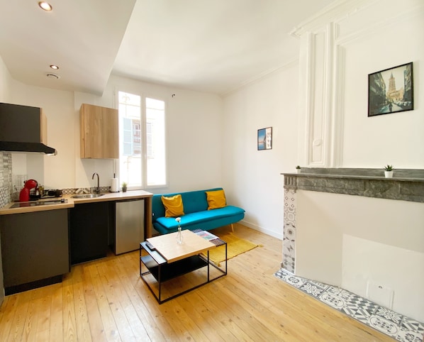 A compact living space with a kitchenette, a blue sofa with yellow cushions, a small table, and a fireplace.
