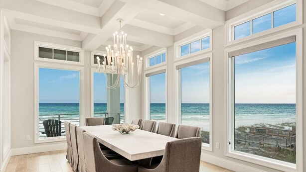 A dining area with a large table and chairs, large windows with ocean views, and a chandelier. - Gulf-Front with Rooftop Deck, Theater and Pool (Miramar Beach)