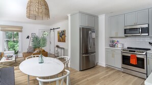 A modern kitchen with a stainless steel refrigerator, a microwave, and an oven. There is a dining area with a white table and chairs. - Cottontail Cottage | Pet-friendly, Fire Pit & 10 Min. to Downtown AVL! (Asheville)