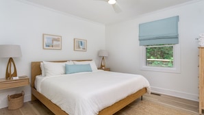 A bedroom with a wooden bed, two bedside tables, a ceiling fan, and a window with a view of greenery. - Cottontail Cottage | Pet-friendly, Fire Pit & 10 Min. to Downtown AVL! (Asheville)