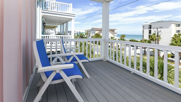Ein Balkon mit zwei blauen Lounge-Stühlen, einem weißen Geländer und Blick auf das Meer sowie andere Gebäude.