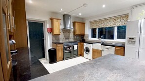Une cuisine moderne avec des meubles en bois, des appareils en acier inoxydable, un four encastré, un lave-linge et un réfrigérateur.