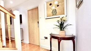 Un escalier avec des balustrades en bois, une porte en bois, un mur blanc, une œuvre d’art encadrée et une petite table avec une plante.