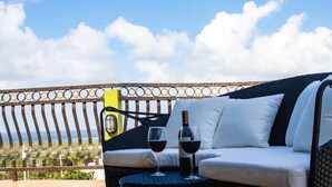 Ein Balkon mit einer Rattan-Couch, zwei Weingläsern und einer Weinflasche.
