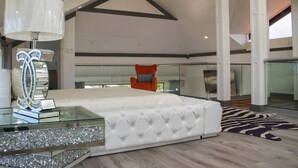 Ein geräumiges Schlafzimmer mit einem großen Bett, einem Glastisch und einer modernen Pendelleuchte.