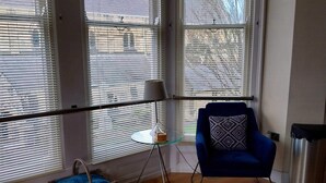 Une pièce dotée de grandes fenêtres, d’un fauteuil bleu, d’une table en verre et d’un panier en osier.