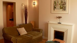 Ein Wohnzimmer mit einer Couch, einem Kamin, einem gerahmten Bild und einer Vase mit hohen Pflanzen.