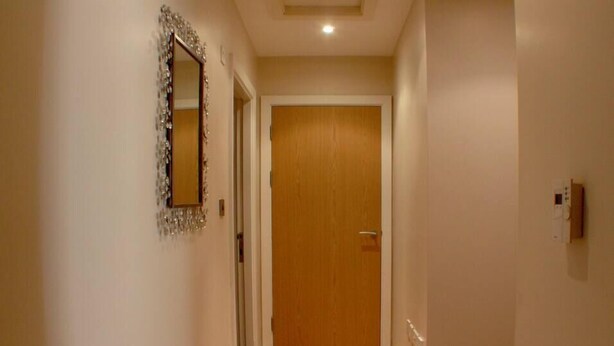 Ein Korridor mit einer Holztür am Ende, einem Spiegel mit dekorativem Rahmen und einem Thermostat an der Wand.