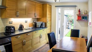 A kitchen with wooden cabinets, a dining table, and chairs. There is a toaster, a kettle, and a microwave on the counter.