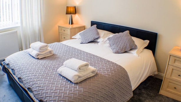 A neatly made bed with a patterned bedspread, two pillows, and two folded towels on the side.