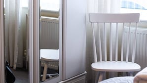 A room with a white chair, a small table, and a mirror reflecting a window and radiator.