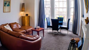 Ein gemütliches Wohnzimmer mit einem braunen Ledersofa, einem Holztisch und einem Essbereich mit blauen Stühlen und einem Tisch.
