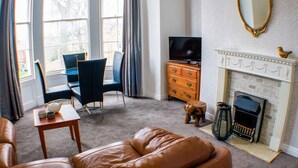 Ein Wohnzimmer mit einer Ledersofa, einem Fernseher, einem Kamin und einem Essbereich mit Stühlen.