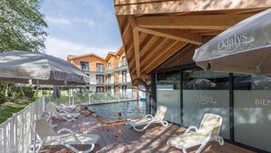A poolside area with lounge chairs and umbrellas, a wooden deck, and a view of a building with balconies. - Wifi, fitness, swimming pool, sauna, hammam, parking, tv, 34m², Chamonix (Chamonix-Mont-Blanc)