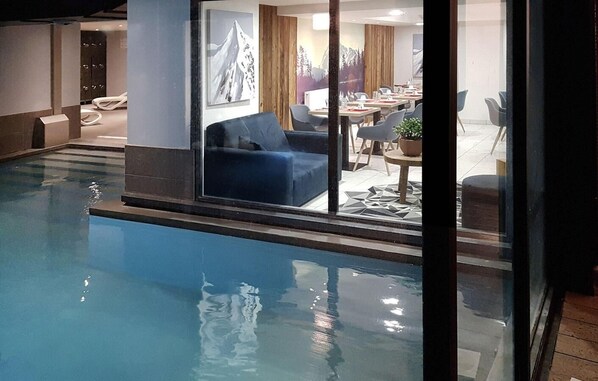 A swimming pool adjacent to a dining area with a view of a mountain range.