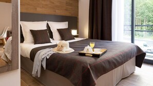 Quarto de hotel moderno com uma cama grande, cabeceira de madeira e vista para o exterior através de uma janela ampla.