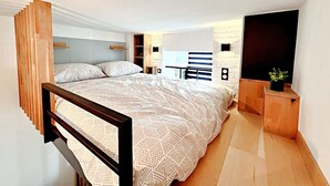 Un dormitorio moderno con cama, cabecera de madera, estanterías empotradas, un escritorio pequeño y una planta en maceta.