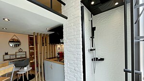 Una cocina moderna con estufa integrada, un comedor con mesa y sillas, y un área de ducha con puerta de vidrio.