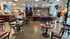 Interior de restaurante com mesas, cadeiras, área de bar e uma tela de televisão.
