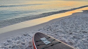 Cena de praia com uma prancha de surf e um caiaque na areia.